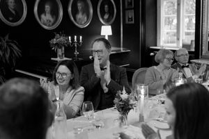 Black and white candid photo of wedding guests laughing and enjoying themselves at a reception dinner table.