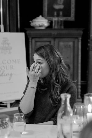 A candid black and white photo of someone sitting at a dinner table with candles and glassware.