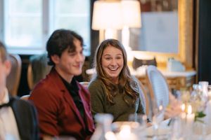 People enjoying conversation and laughter during a social gathering at a restaurant table with warm lighting.