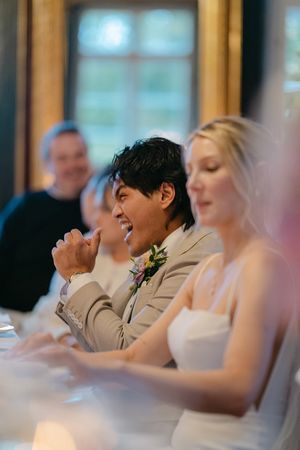 Wedding guests seated at a table laugh and share joyful moments during a reception celebration.