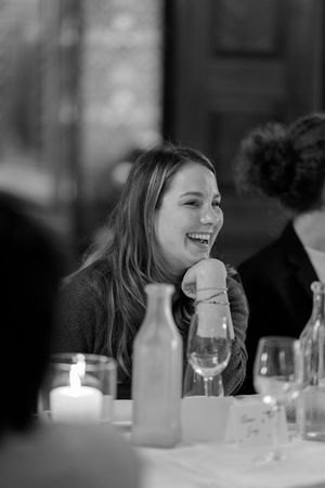 A candid black and white photo of someone laughing at a dinner table with wine glasses and candles.