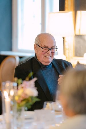 Smiling guest wearing glasses and a blue sweater sits at an elegant dinner table with candlelight and floral decor.