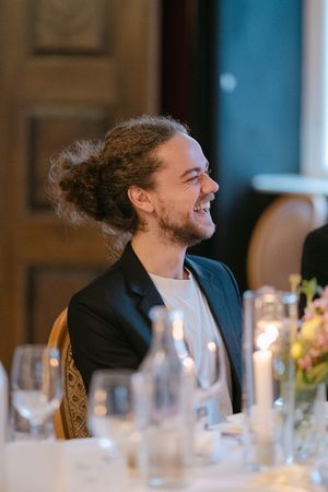 Guests laugh and smile during a formal dinner event with elegant place settings and glassware on the table.