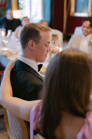 Wedding guests seated at elegant candlelit dinner tables in formal reception setting.