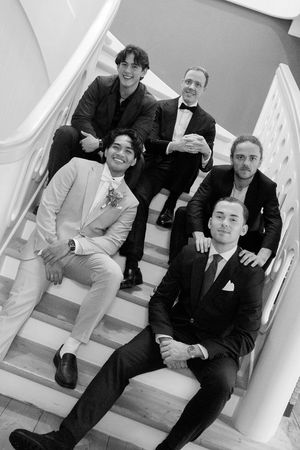 A group of formally dressed people sitting and standing on white stairs in a black and white photograph.
