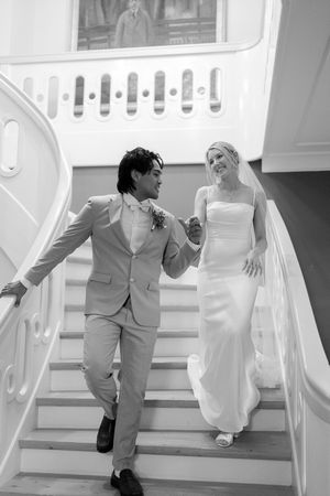 A black and white photo series shows a couple in wedding attire playfully running up white stairs together.