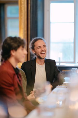 People enjoying a lively conversation while dining at a table with wine glasses in an elegant indoor setting.