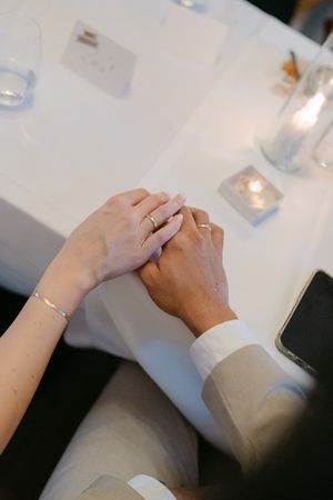 Two people hold hands intimately across a white table in a romantic gesture.