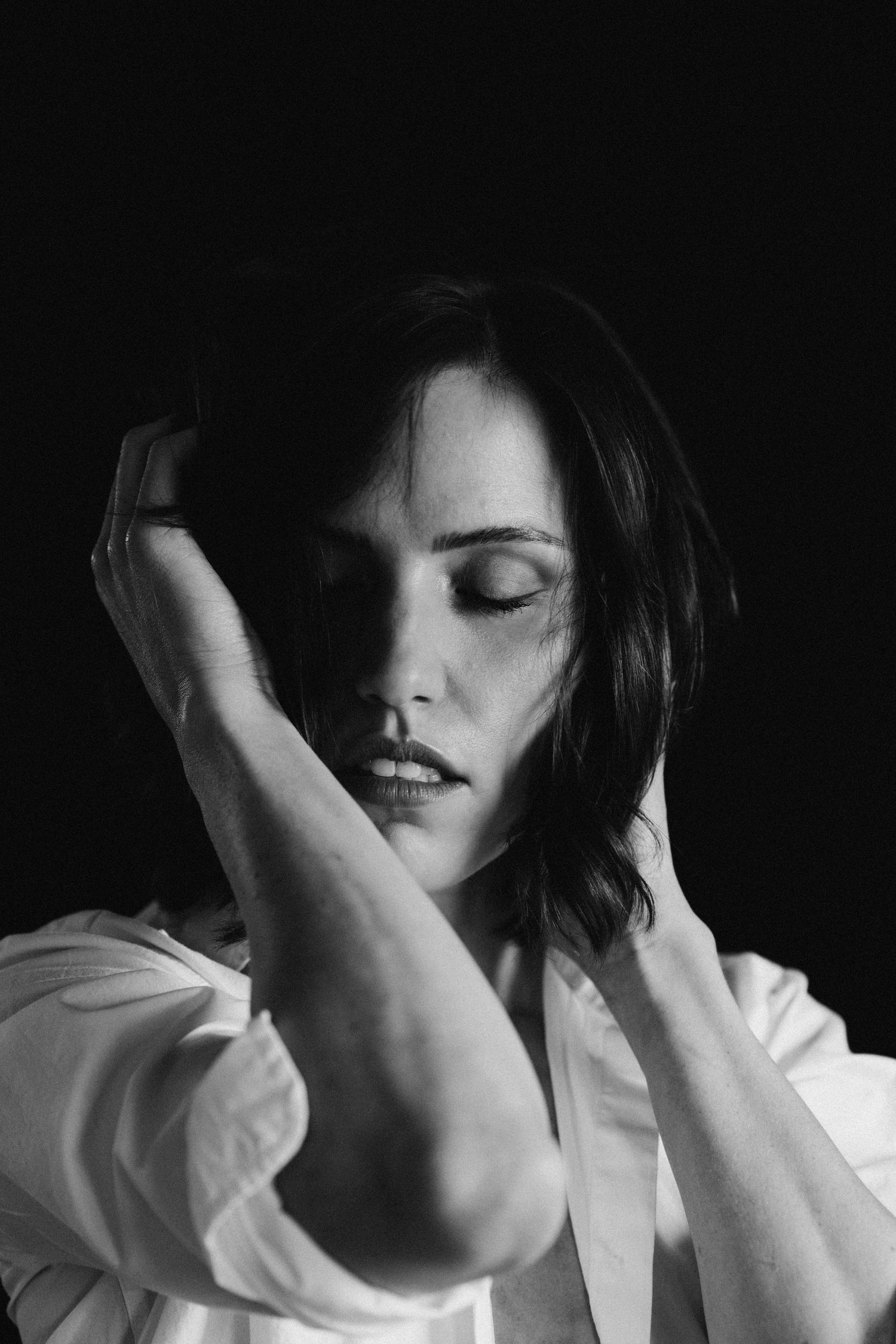 Black and white moody portrait of dark-haired woman with closed eyes and hands framing her face.