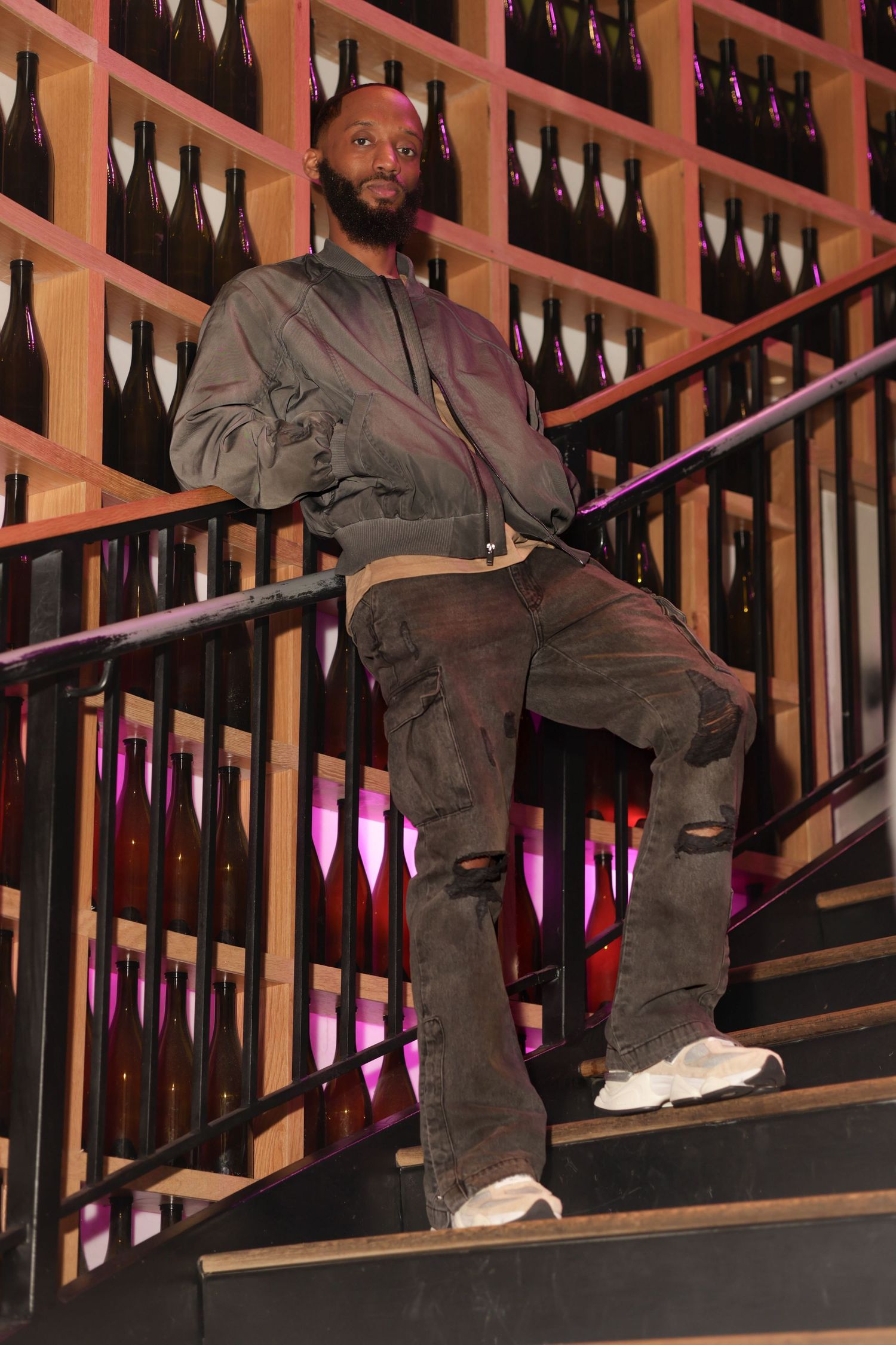 A person wearing gray clothing sits casually on dark stairs with illuminated purple lighting visible in the background.