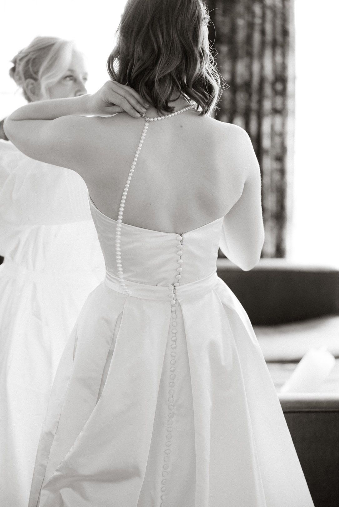 Close-up black and white view of wedding dress details showing pearl buttons and elegant fabric texture.
