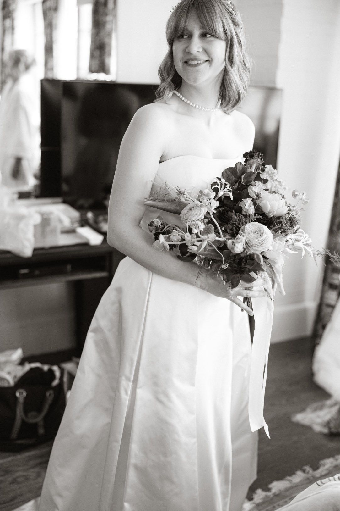 A bride in a classic white strapless wedding gown holds a beautiful bouquet of mixed flowers in black and white.