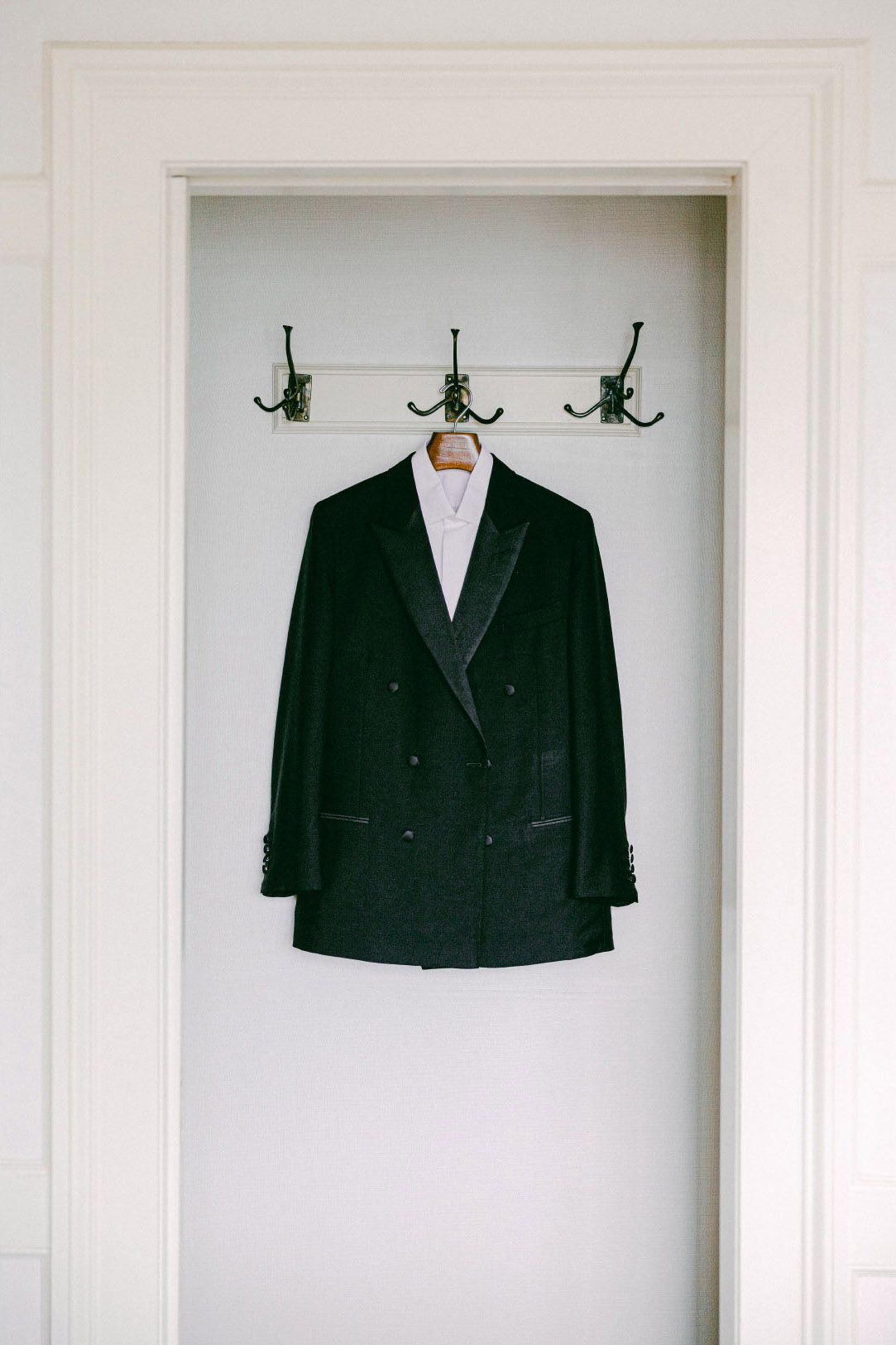 A black suit jacket hangs on a white wall in a minimalist display setting.