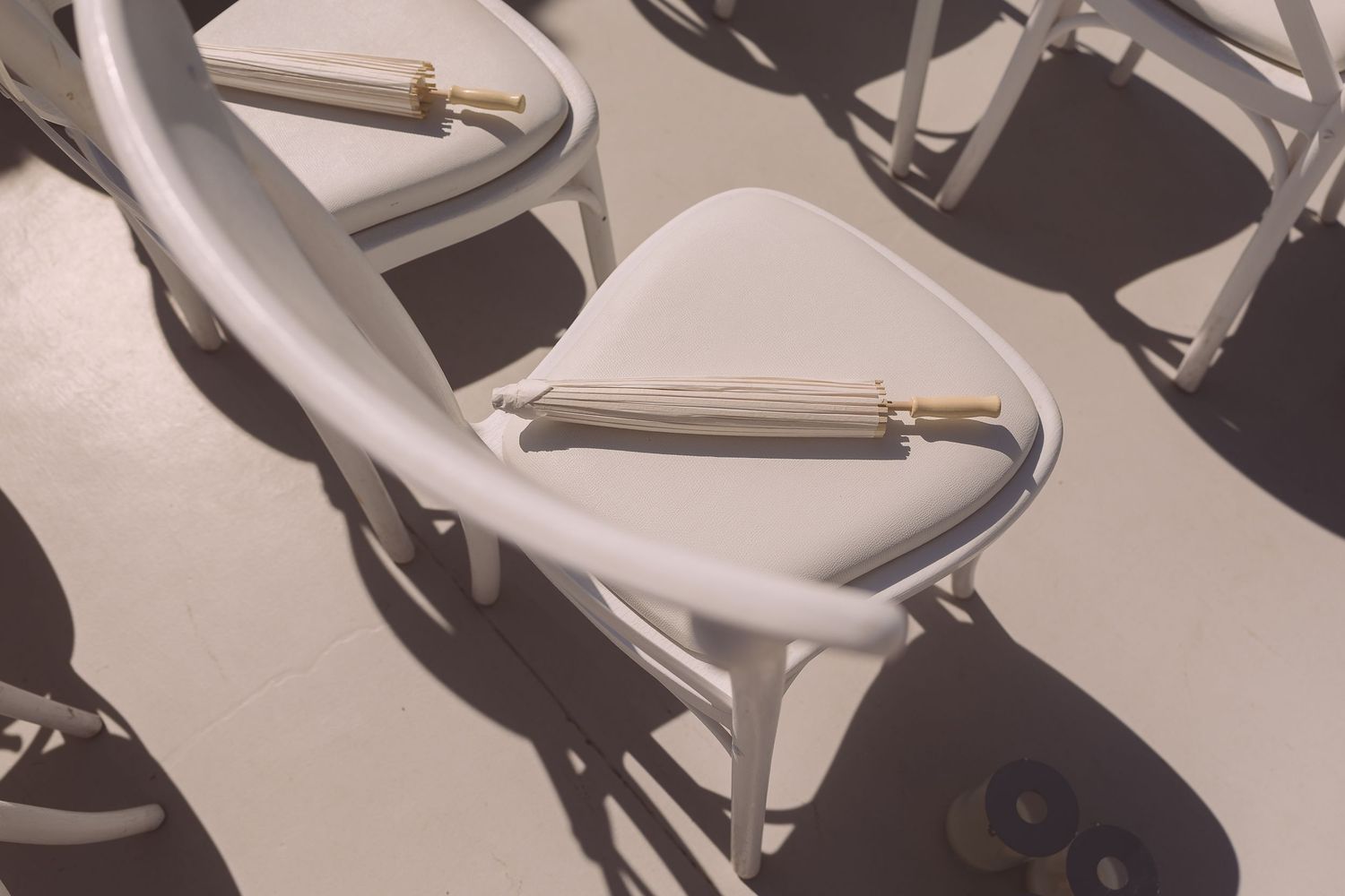 White wooden chairs in sun with white parasols laid on the seats.