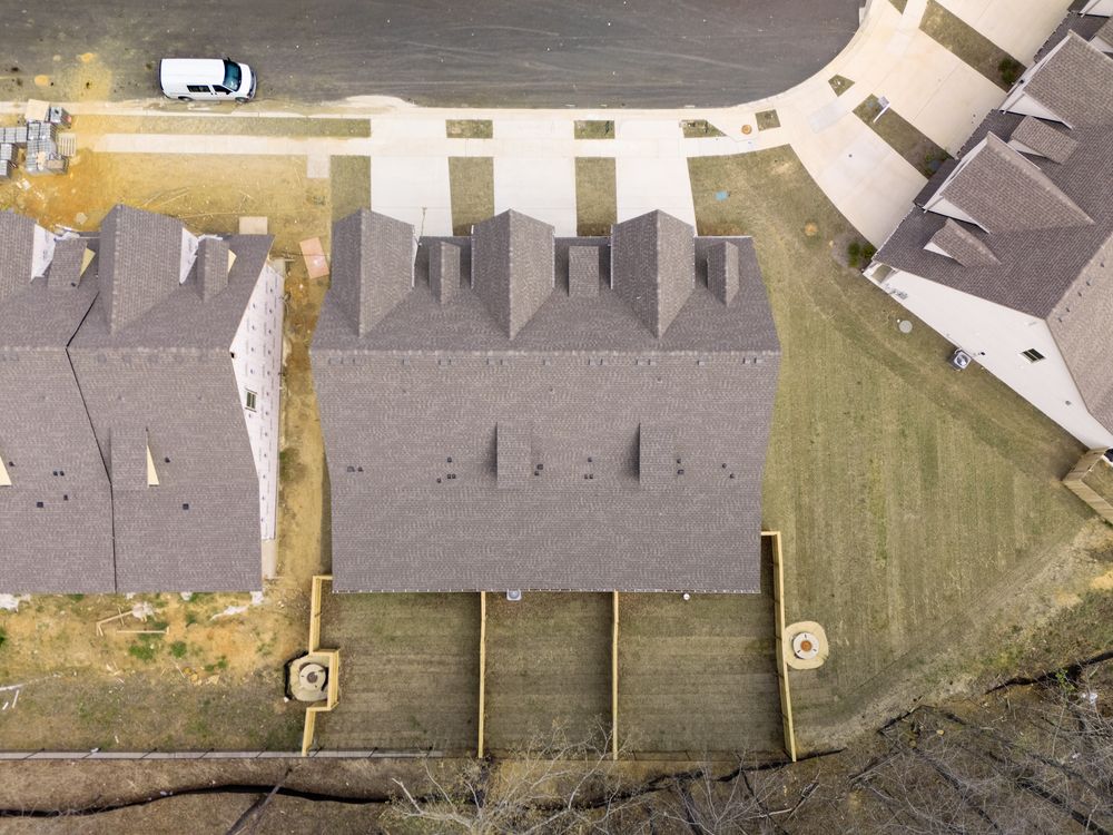 Aerial view of new construction townhomes with gray roofs in a residential development surrounded by open land.