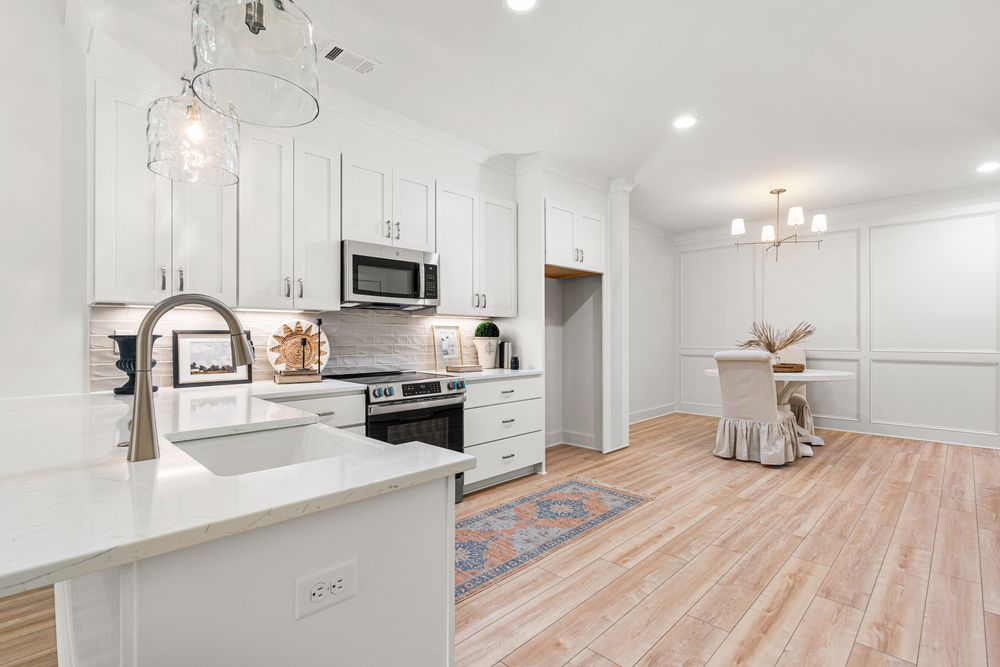 Modern white kitchen with stainless steel appliances, quartz countertops, pendant lights, and light hardwood floors.