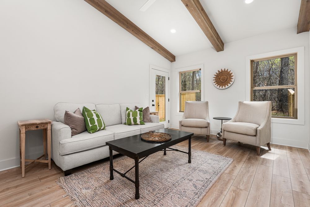 Bright living room with vaulted wood beam ceiling, white sofa, black coffee table, and hardwood floors.