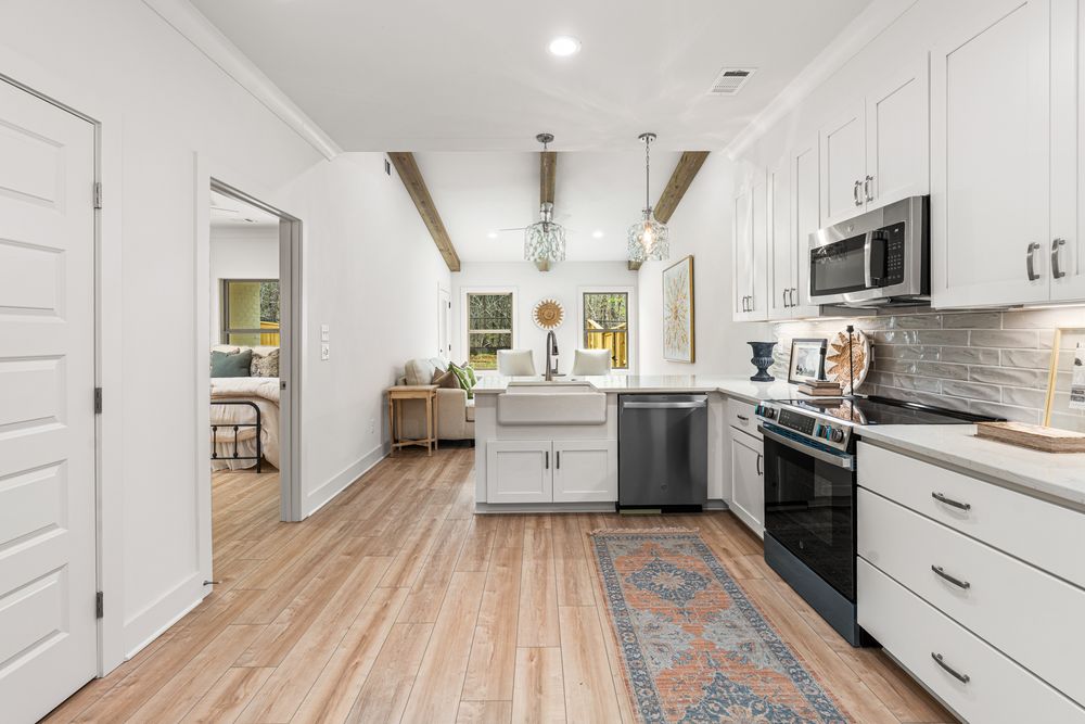 Modern white kitchen with farmhouse sink, stainless steel appliances, subway tile backsplash, and hardwood floors.