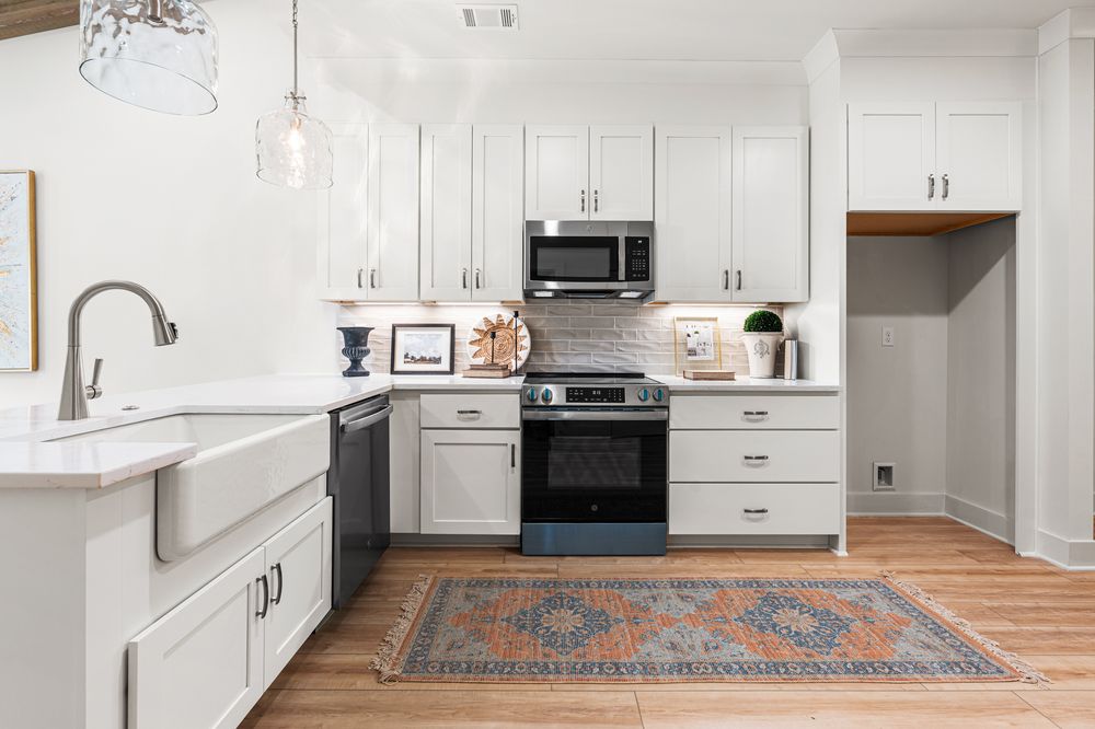 Modern white kitchen with stainless steel appliances, farmhouse sink, gray subway tile backsplash, and hardwood floors with decorative rug.