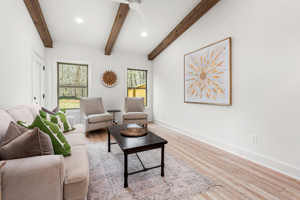 Bright living room with wood beam ceiling, light hardwood floors, neutral sofa, two chairs, and modern wall art.