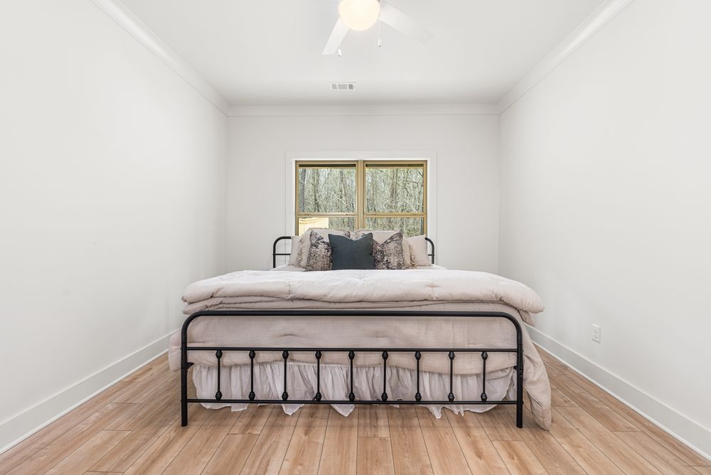 Minimalist bedroom with black metal bed frame, light hardwood floors, and a window overlooking trees.