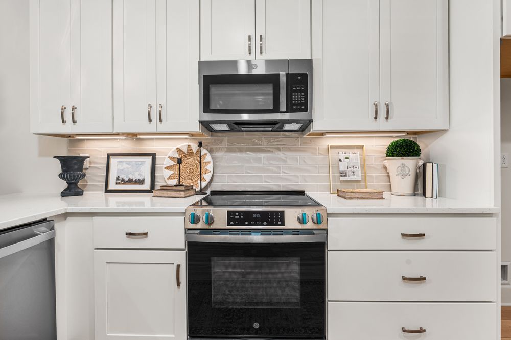 White kitchen cabinets with stainless steel range and microwave, gold hardware, and decorative backsplash tile.