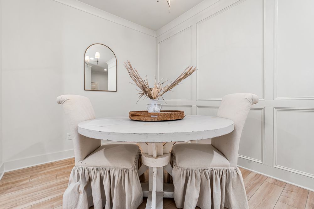 Elegant dining nook with round white table, upholstered skirted chairs, wainscoting, and light hardwood floors.