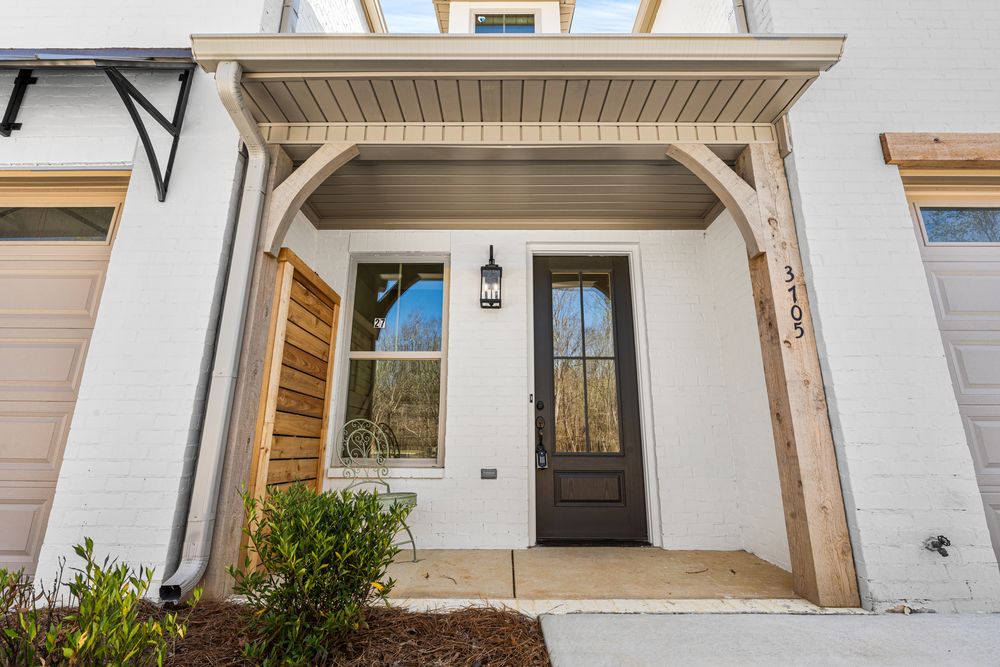 White townhome entrance with dark wood front door, arched pergola, and covered porch with pendant light.