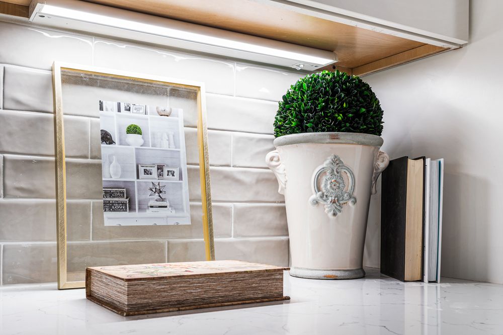 Kitchen counter vignette with framed art, topiary plant, decorative books, and under-cabinet lighting.