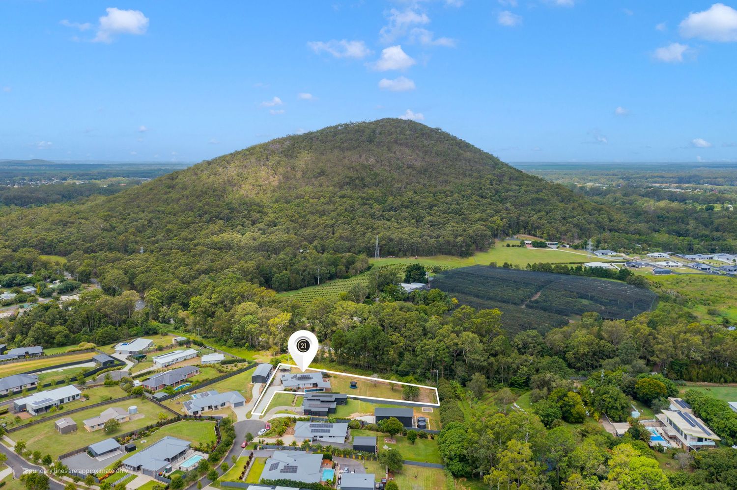 Aerial view of residential property near Glass House Mountains with lush greenery and mountain backdrop in Queensland.