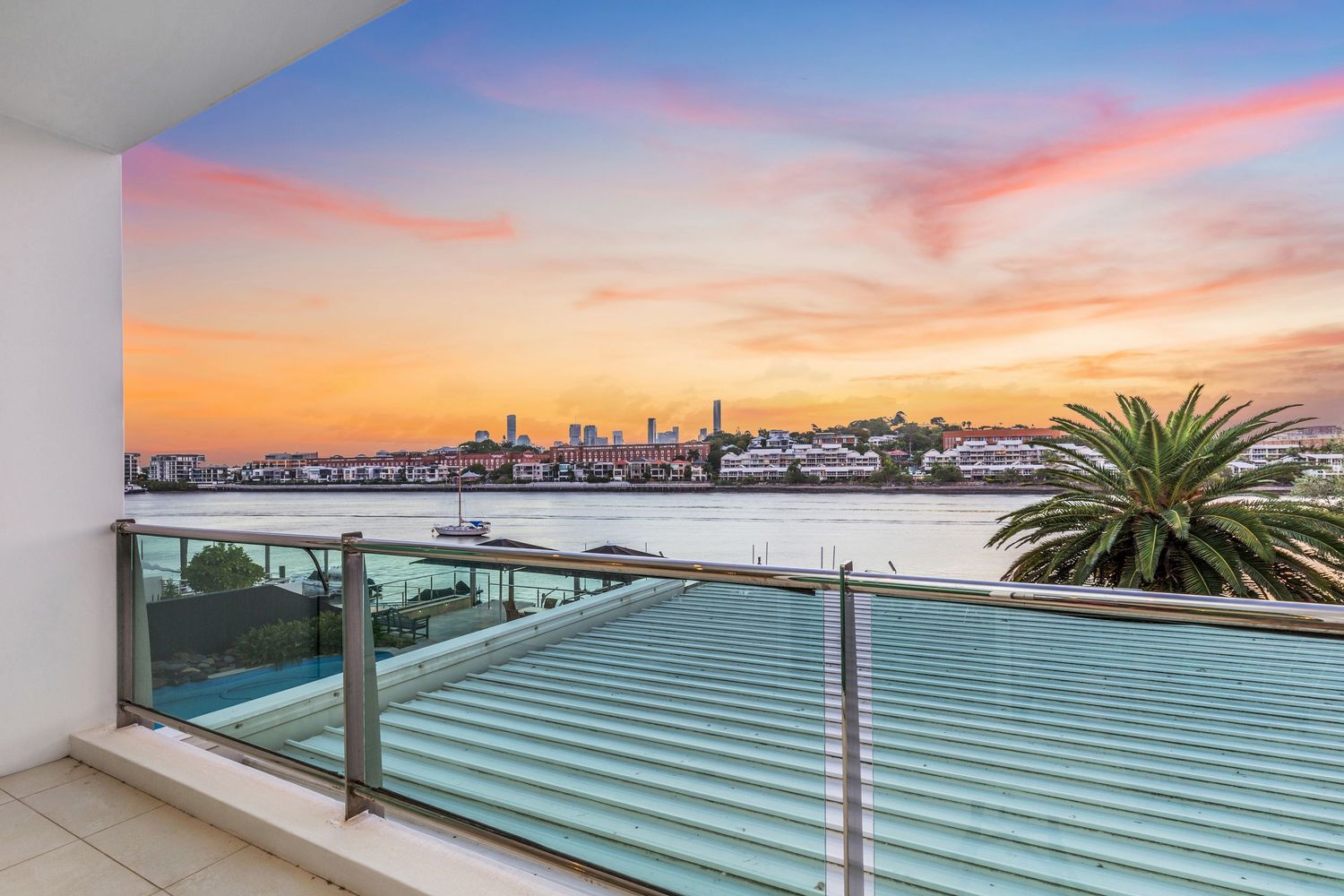 Modern balcony with glass railings offering breathtaking waterfront city views at dusk.