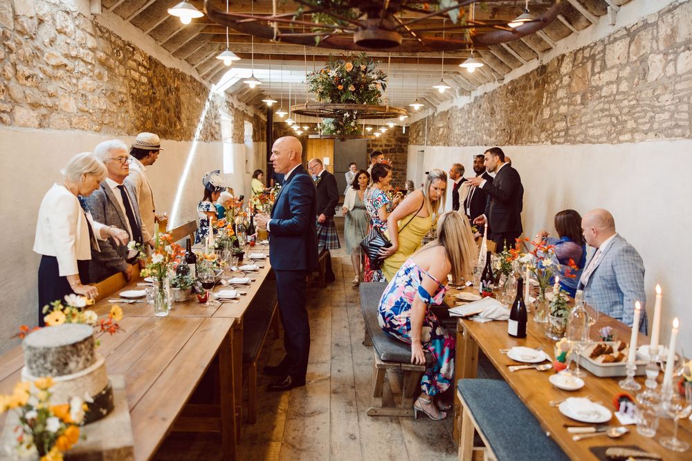 Wedding guests gather at a rustic stone venue with exposed brick walls and wooden beams for an elegant dinner reception.