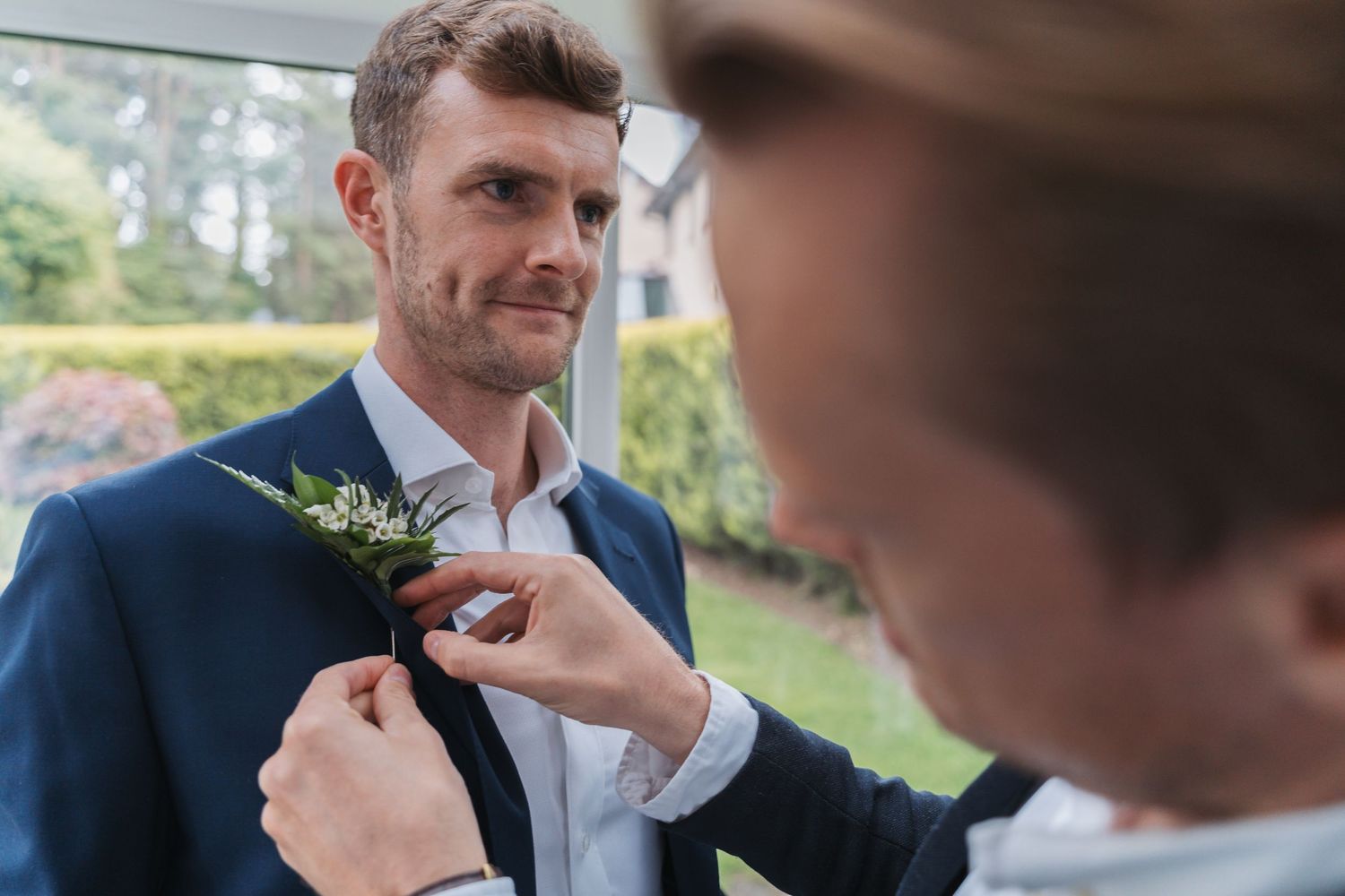 A groom adjusts his tie while getting ready for a wedding ceremony outdoors.