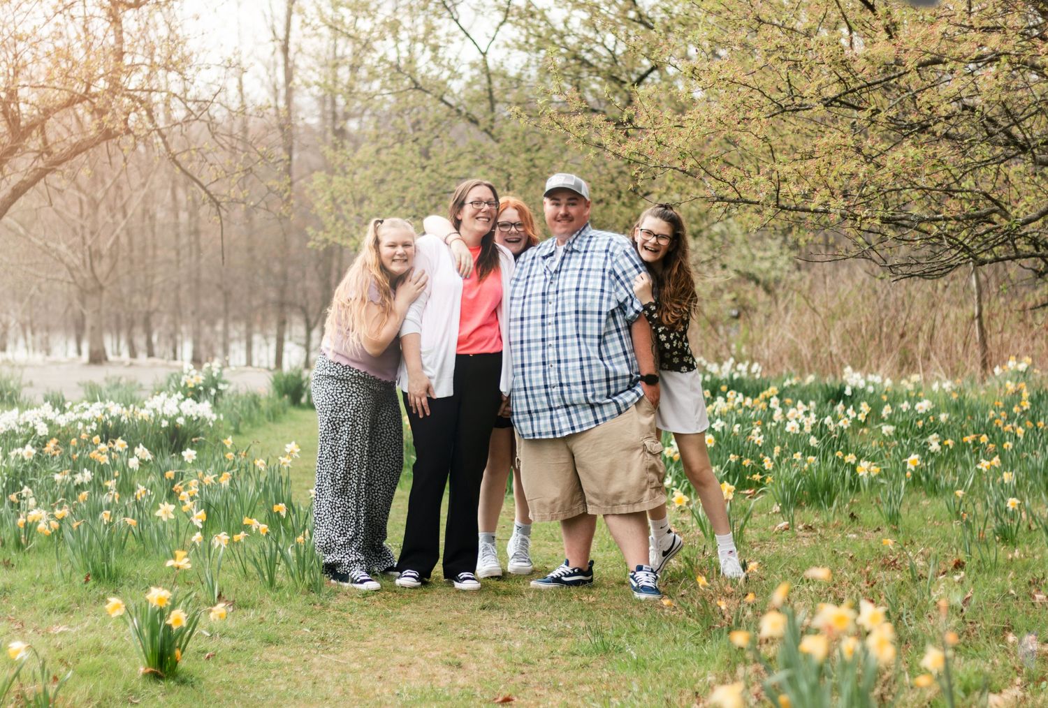A group of people pose together in a spring garden filled with blooming daffodils and trees at sunset.