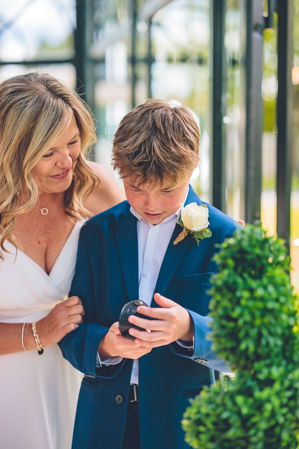 Portrait of a young boy in a blue suit with a white rose boutonniere smiling during a wedding ceremony.