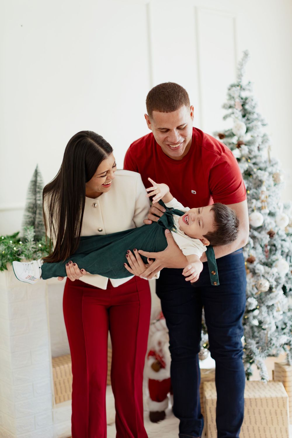 Family playing and laughing together in front of decorated Christmas tree.
