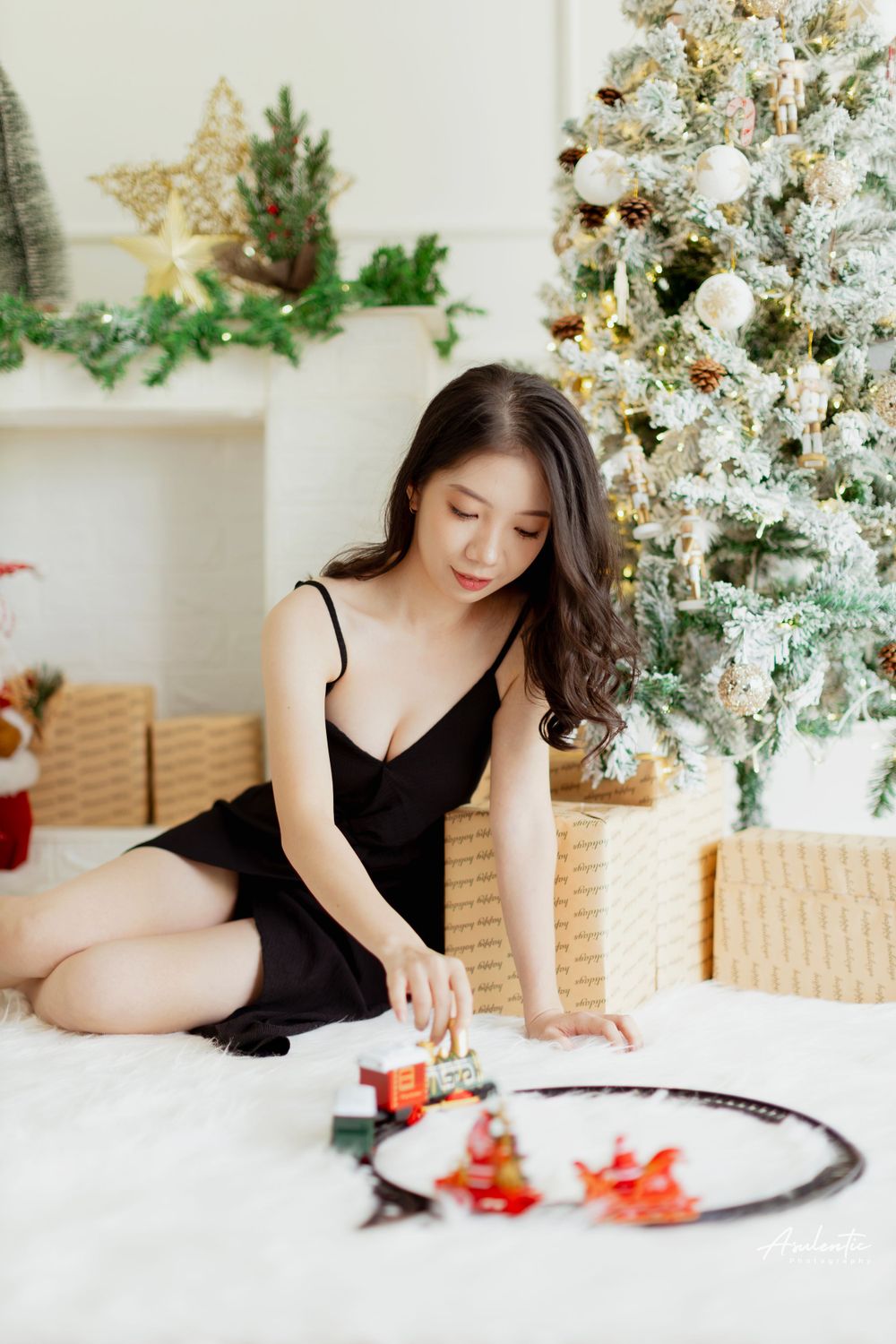 A holiday portrait featuring a black dress and toy train set against a decorated Christmas tree background.
