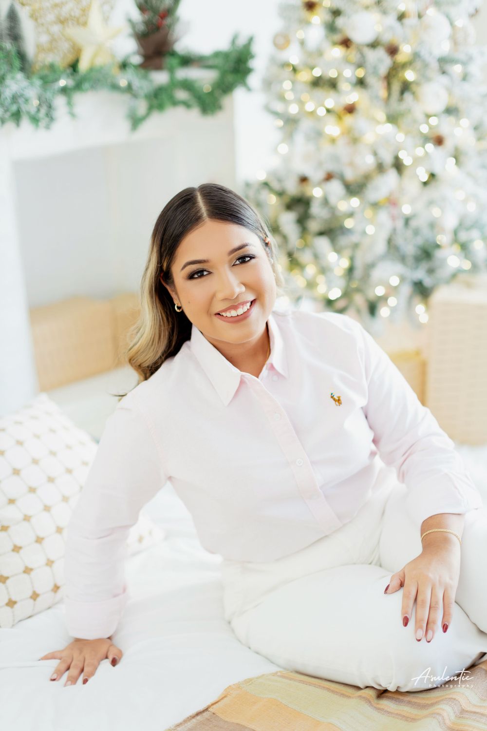 Person in white outfit sits on floor by decorated Christmas tree and holiday decor.