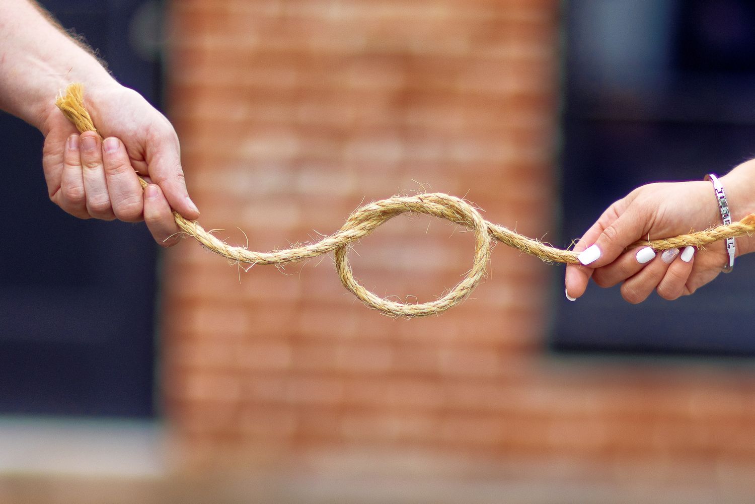 A series of hands passing a rope or string in a horizontal sequence against a dark background.