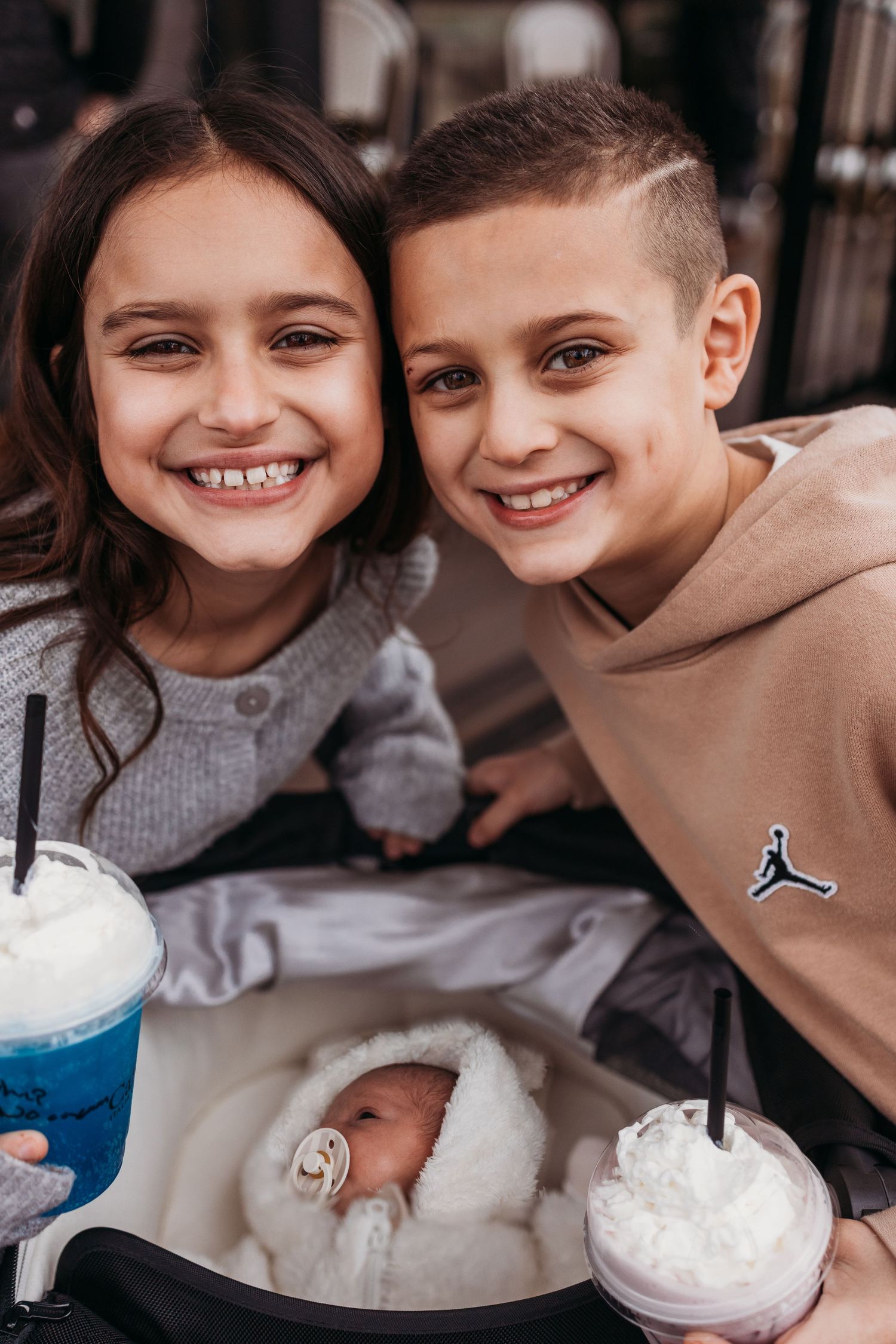 Two smiling children enjoying whipped cream drinks together at a cafe.