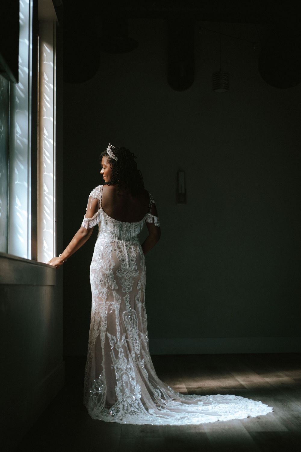 A person in a white lace wedding dress stands in dramatic window light creating a moody silhouette effect. Las Vegas Bride.