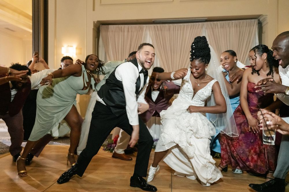 Wedding guests dance and lean backwards in a synchronized line during a fun reception celebration.