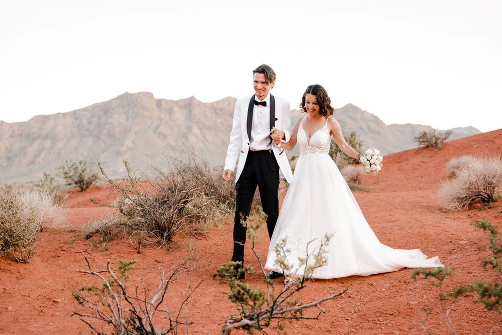A couple poses in white wedding attire against the stunning red rock formations of Valley of Fire State Park at sunset.
