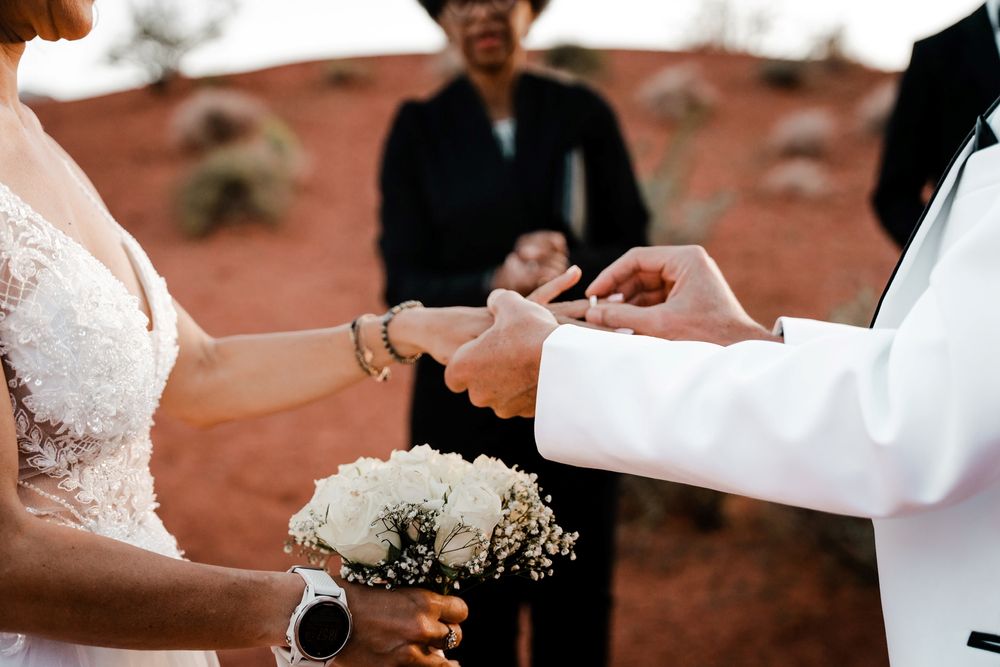 Couple exchanging rings during outdoor wedding ceremony with officiant in background.
