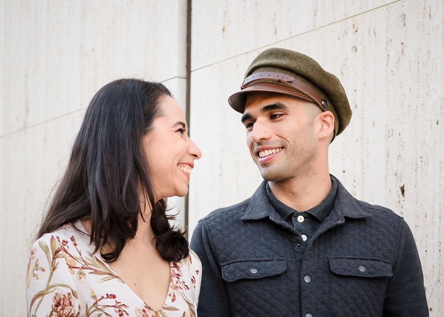 A couple shares a tender moment together while wearing casual attire against a white wall background.