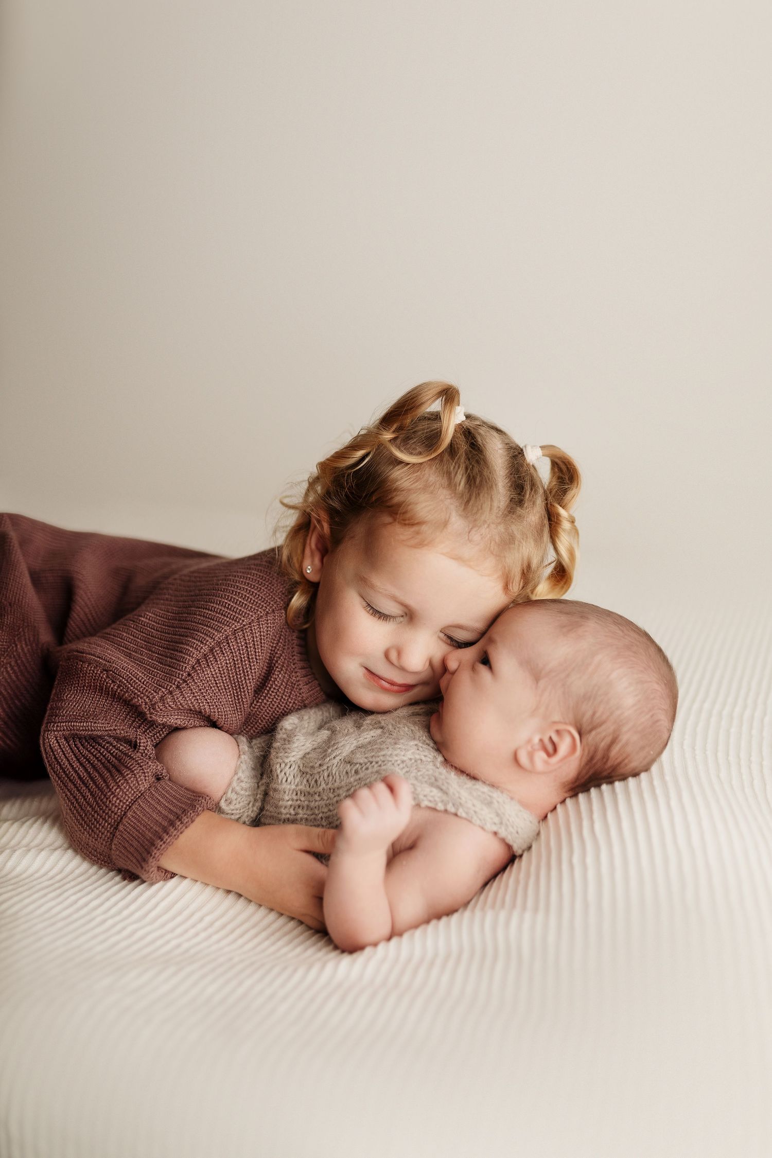 Sweet sibling portrait series showing tender moments between older child and newborn baby on white backdrop.