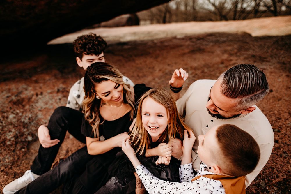 A family sits together outdoors sharing a joyful moment on brown autumn ground.