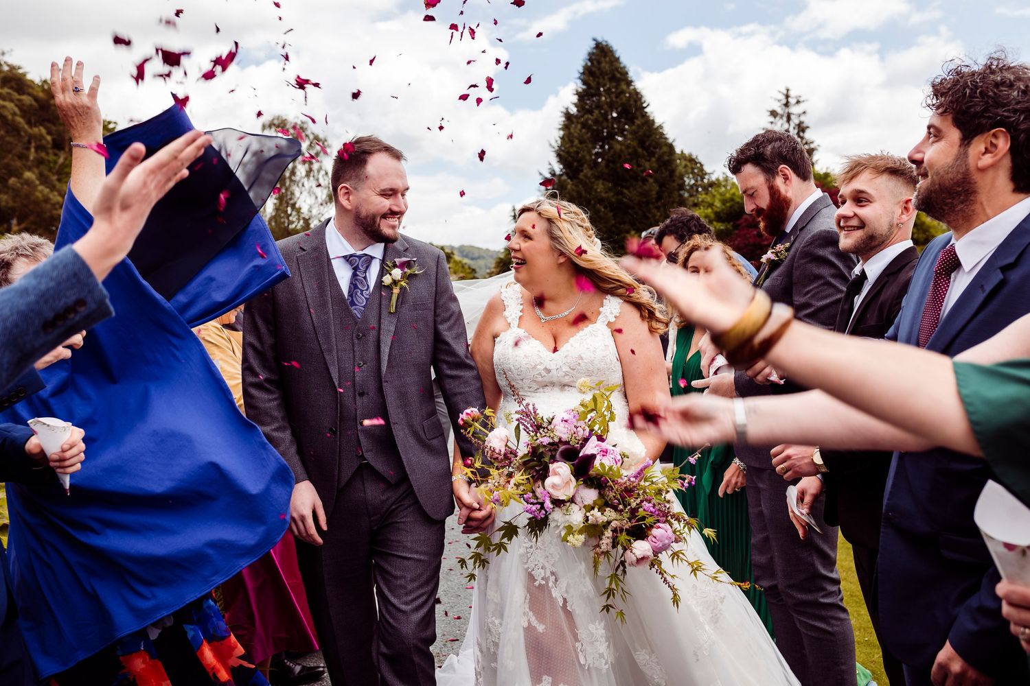 Wedding guests toss colorful flower petals in celebration as newlyweds walk through a joyful confetti shower.