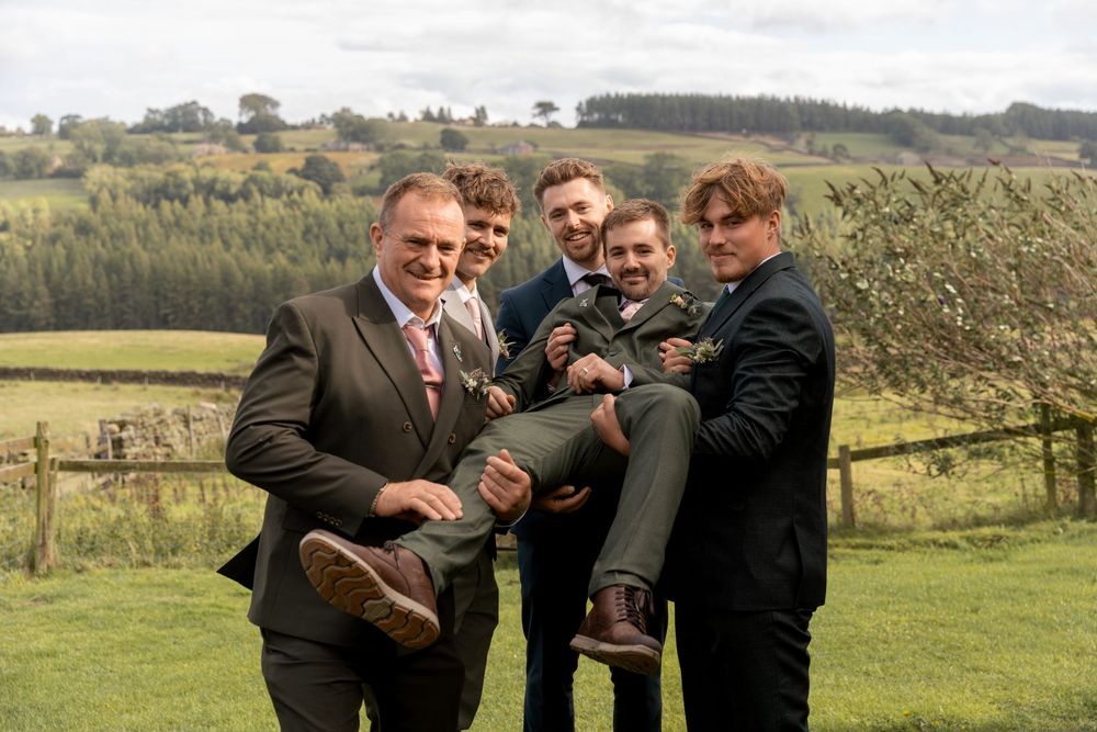 A group of people laughing and embracing in a scenic green countryside setting.