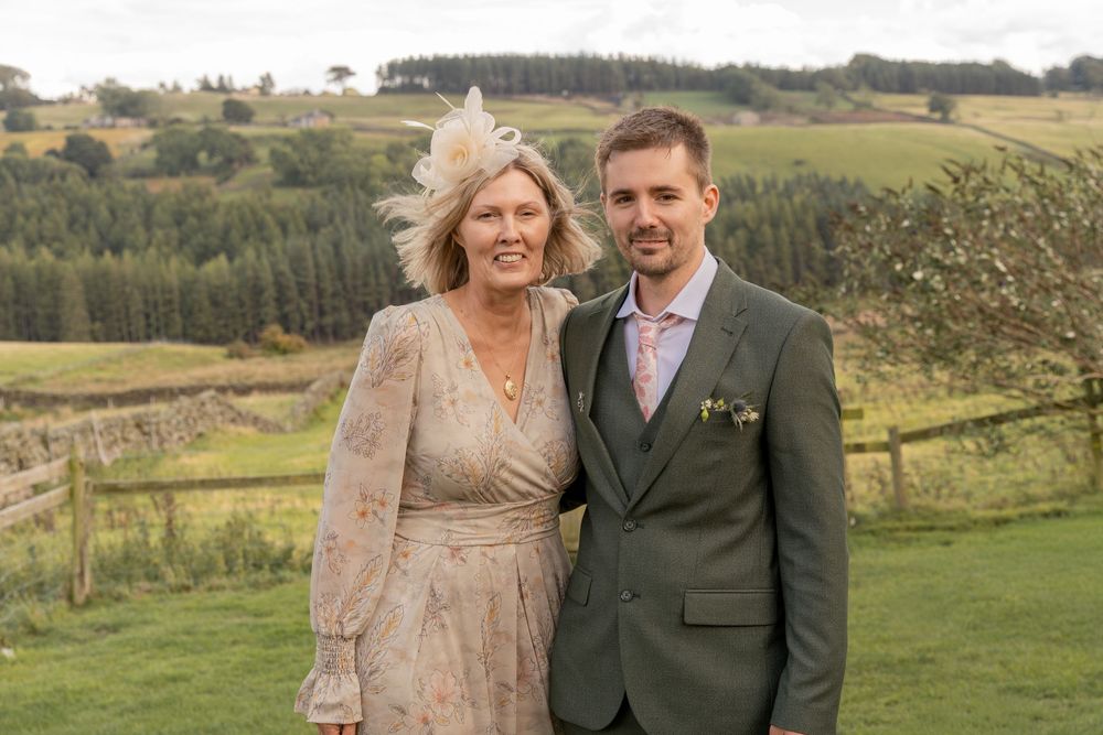 A couple poses together in a rural countryside setting with rolling green hills and fields in the background.